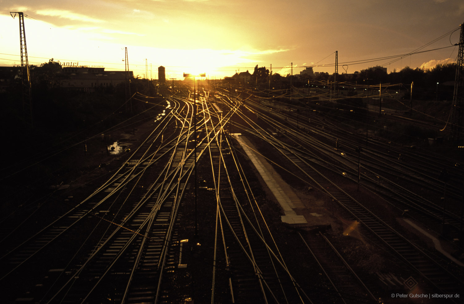 Bahngleise im warmen Licht der untergehenden Sonne. Die Schienen verlaufen parallel und scheinen in der Ferne zusammenzulaufen, während ihr metallischer Glanz das goldene Abendlicht reflektiert.